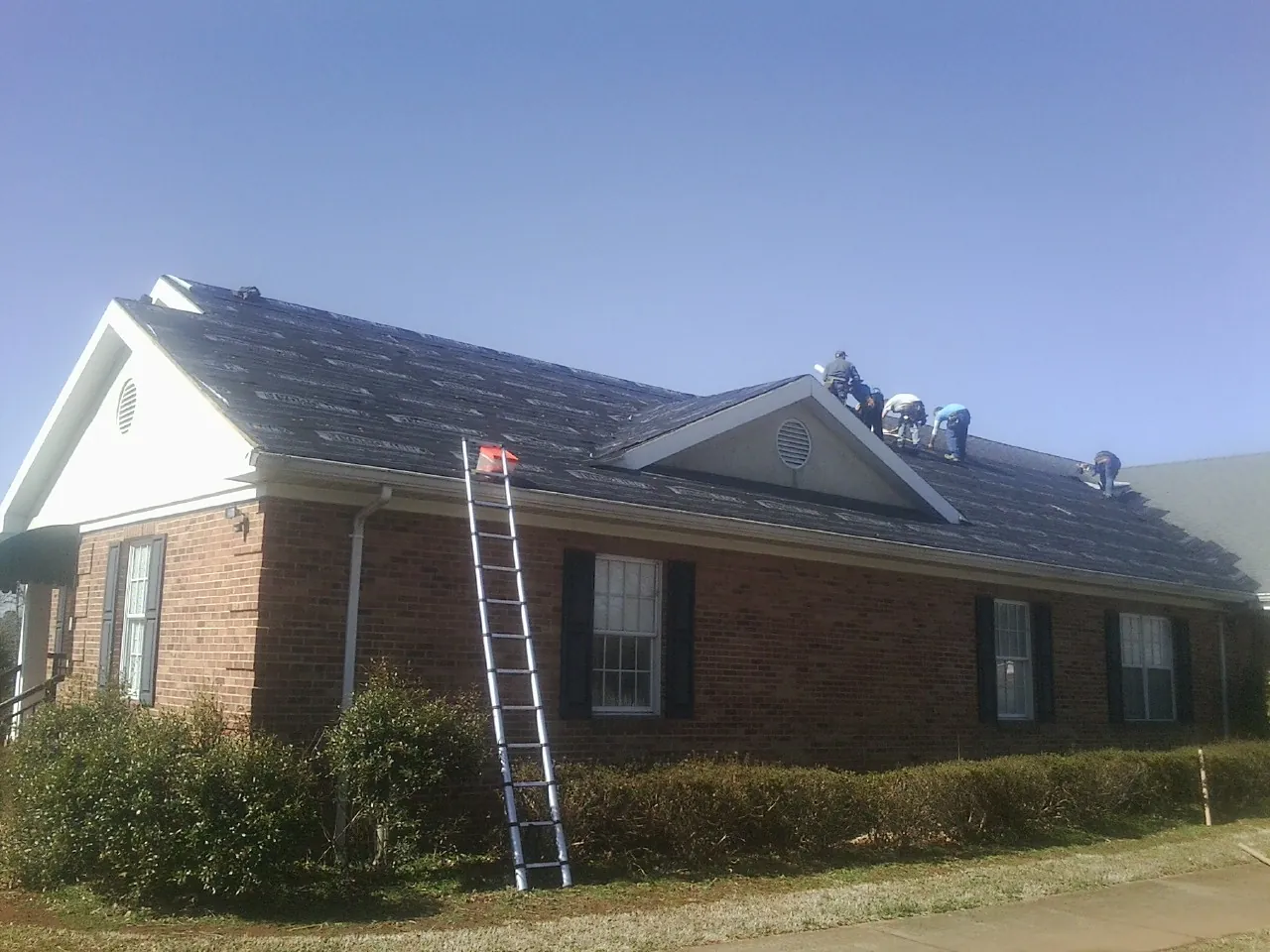 Crew tearing shingles off a brick ranch roof with a ladder set — Emergency Roof Repair work by our crew in East Palatka