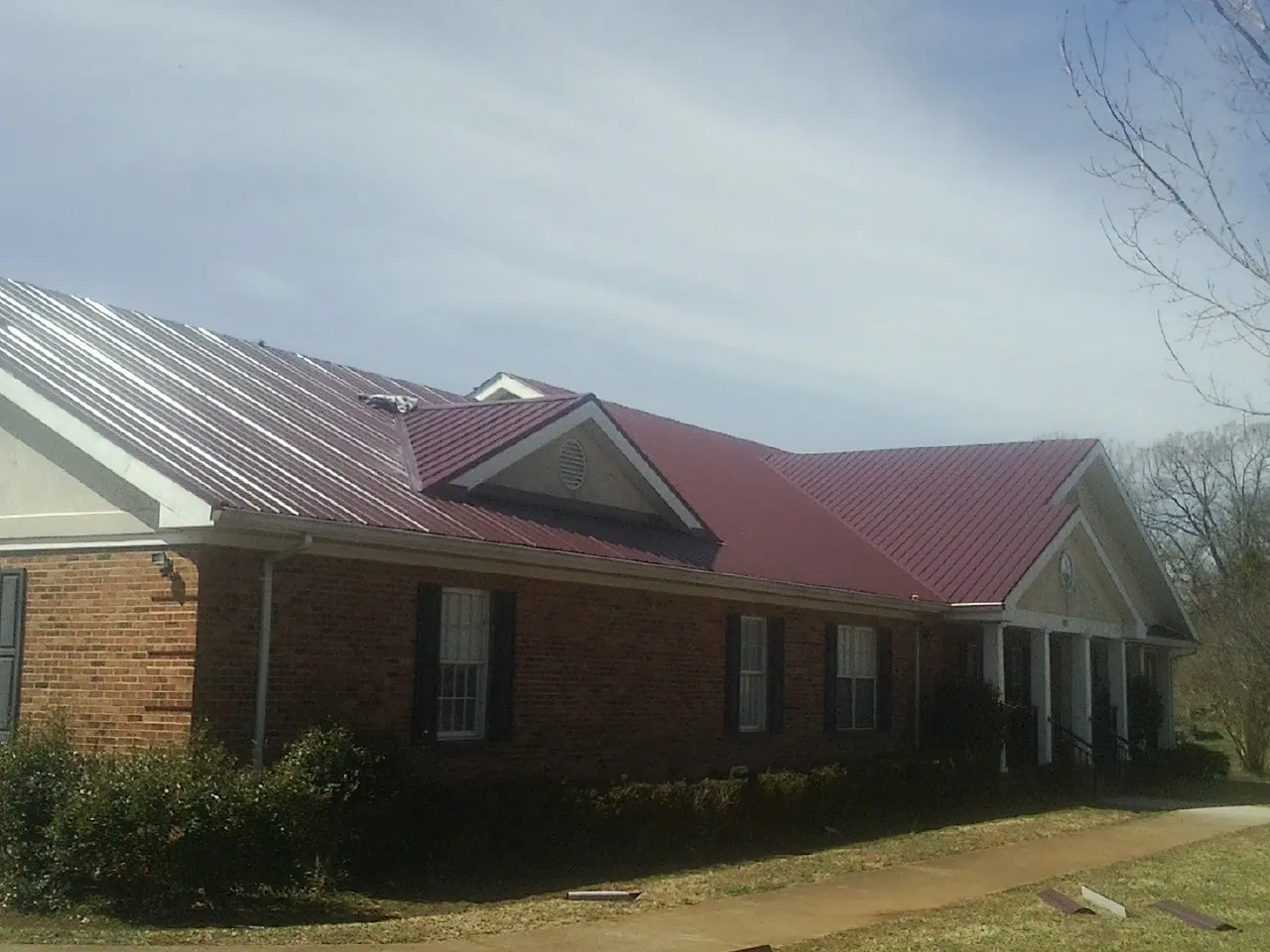 Red metal roof with gabled entries on a long brick building, from a Hail Damage Roof Repair job in East Palatka