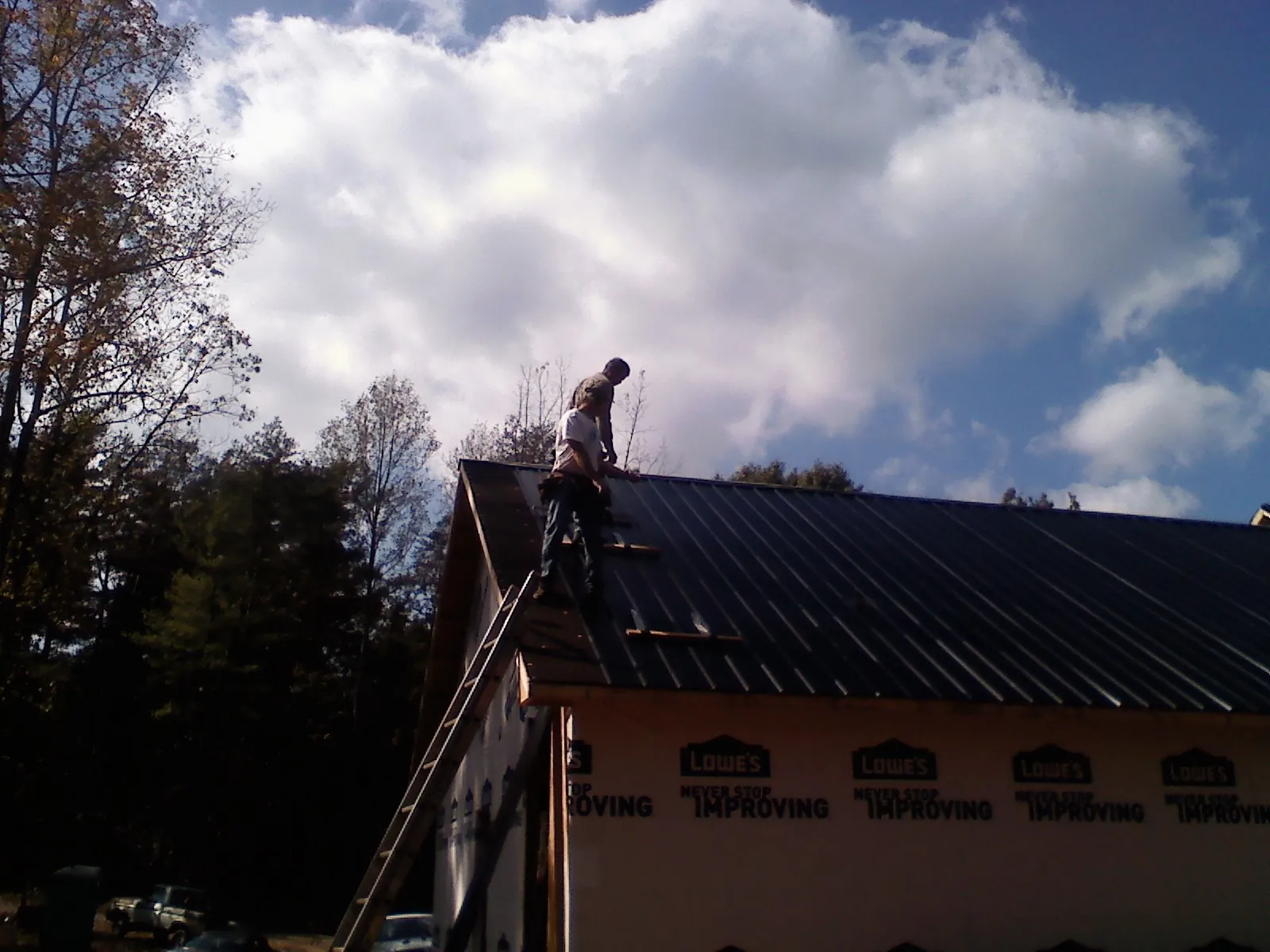 Roofer fastening dark metal panels high against a cloudy sky, from a Roof Inspection job in East Palatka