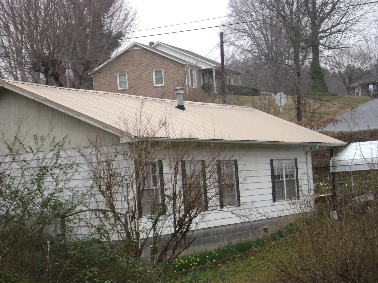 Tan metal roof on a white sided house set into a hillside — Commercial Roofing by Roofing Brothers in East Palatka